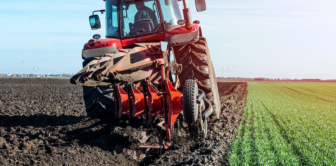 Red modern tractor plowing a large agricultural field under a clear blue sky