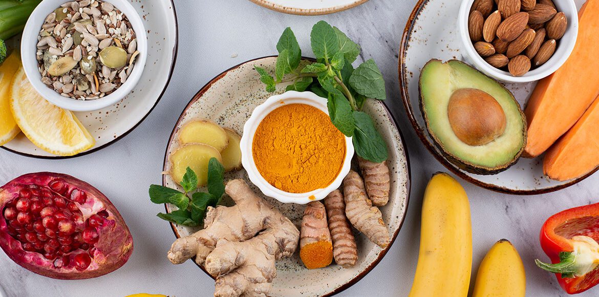 Flat lay of anti-inflammatory superfoods featuring fresh turmeric, ginger, avocado, and mixed nuts for a healthy diet.