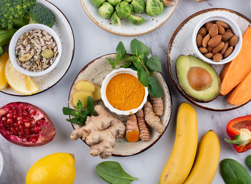 Flat lay of anti-inflammatory superfoods featuring fresh turmeric, ginger, avocado, and mixed nuts for a healthy diet.