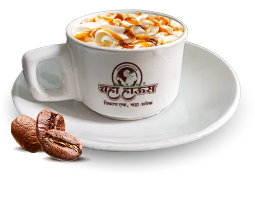 A 'Chaha House' branded white cup and saucer filled with a coffee drink topped with whipped cream and caramel drizzle, shown with roasted coffee beans in the foreground.