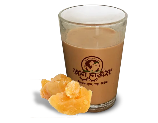 Branded glass of hot jaggery tea (Gulacha Chaha) with raw jaggery pieces on a white background